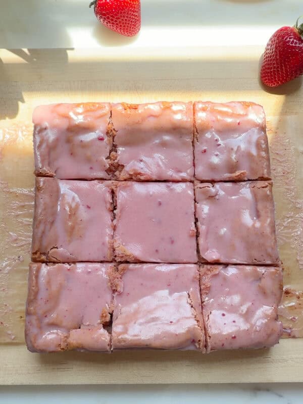 Glazed and sliced strawberry brownies on cutting board.