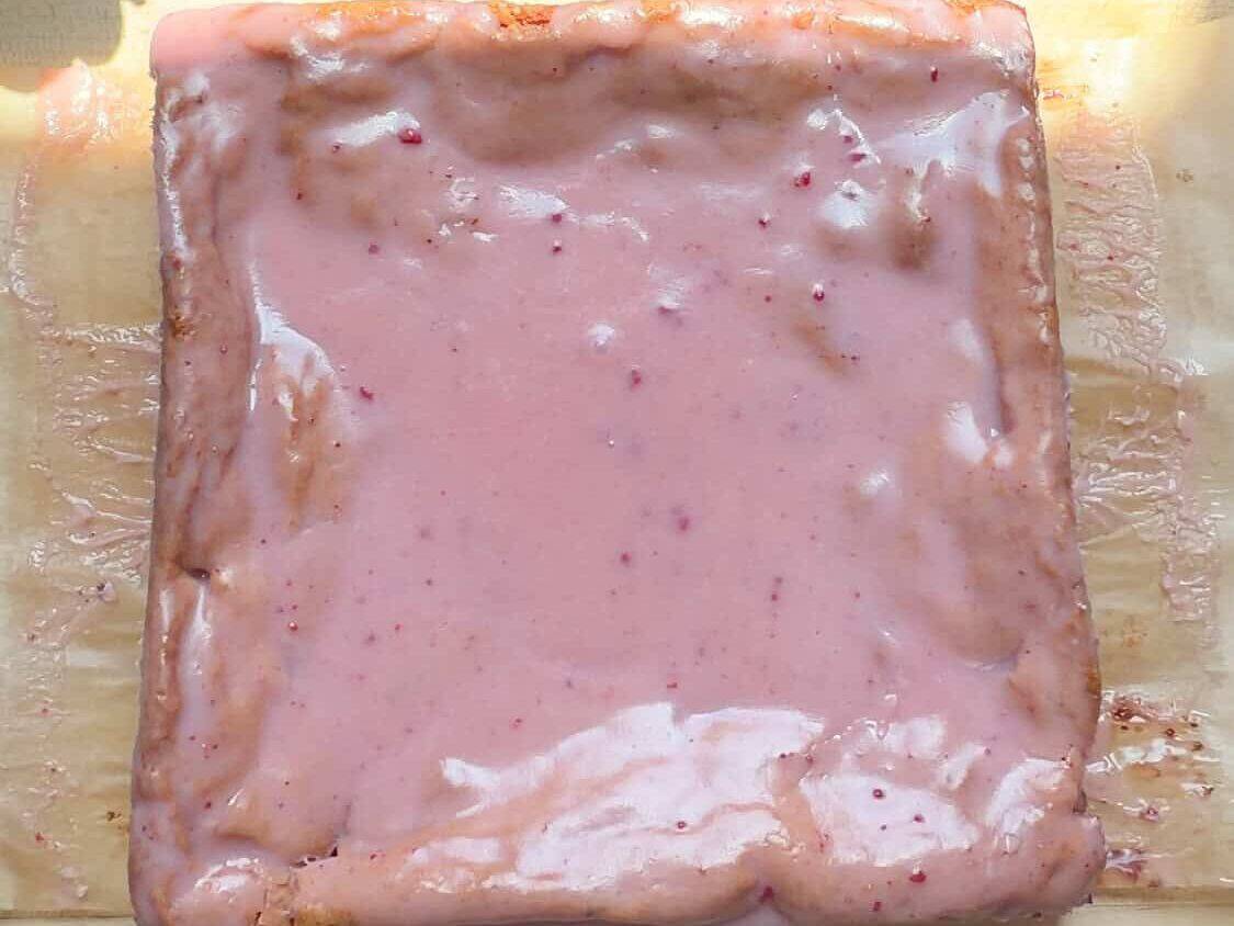 Glazed strawberry brownies on cutting board.