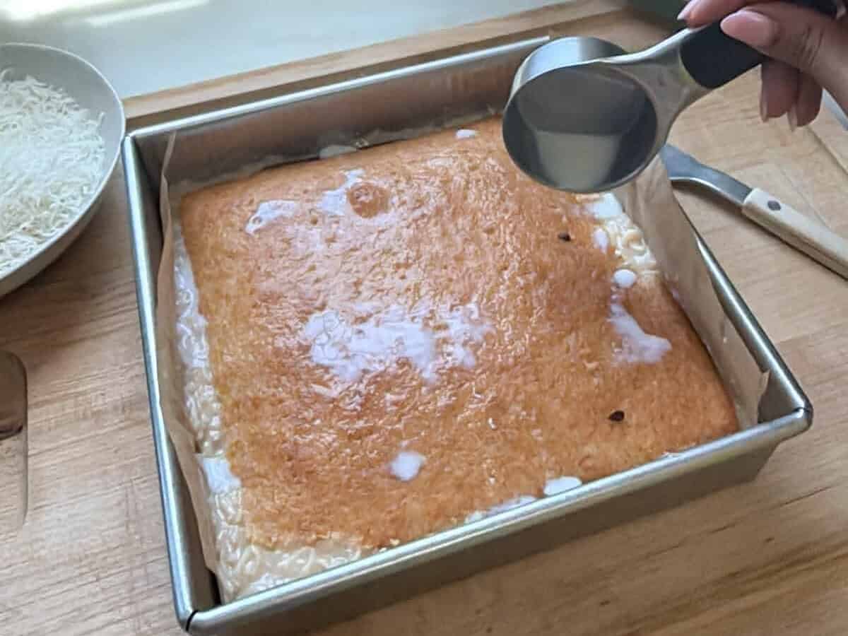Pouring milk over the Bolo de Coco in a baking pan.
