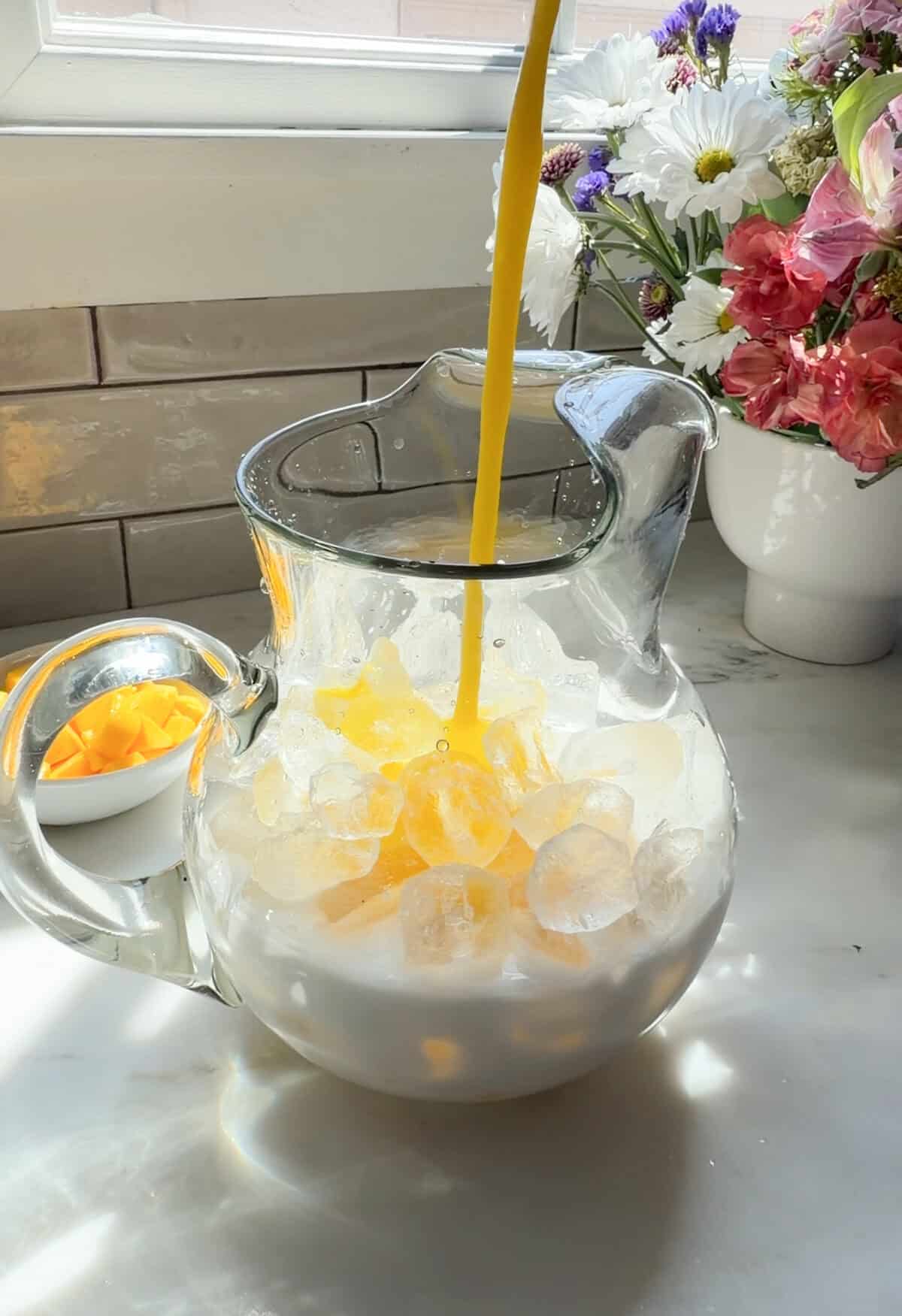 Pouring mango puree into pitcher of ice and coconut milk.