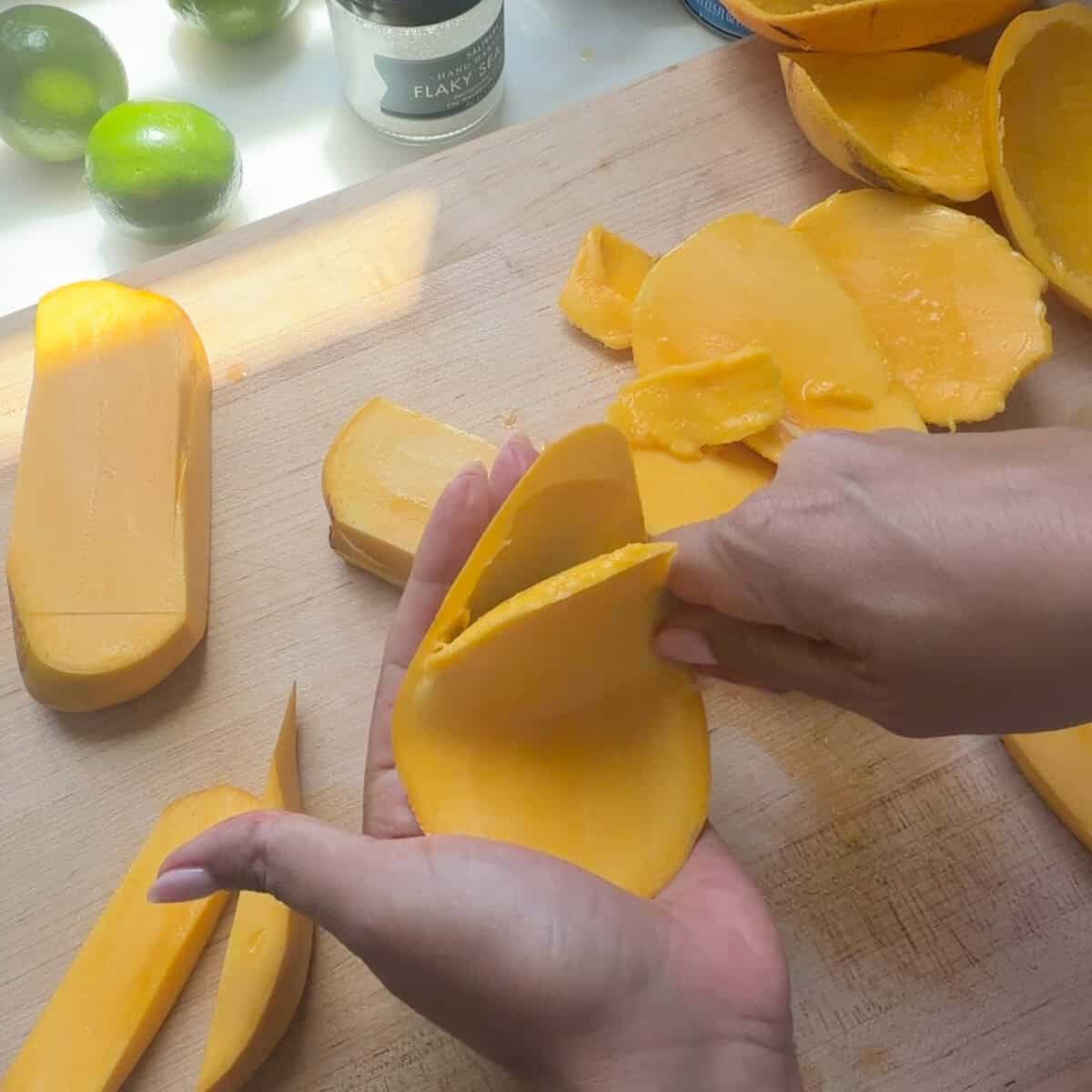 Peeling mangoes and mangoes on cutting board.