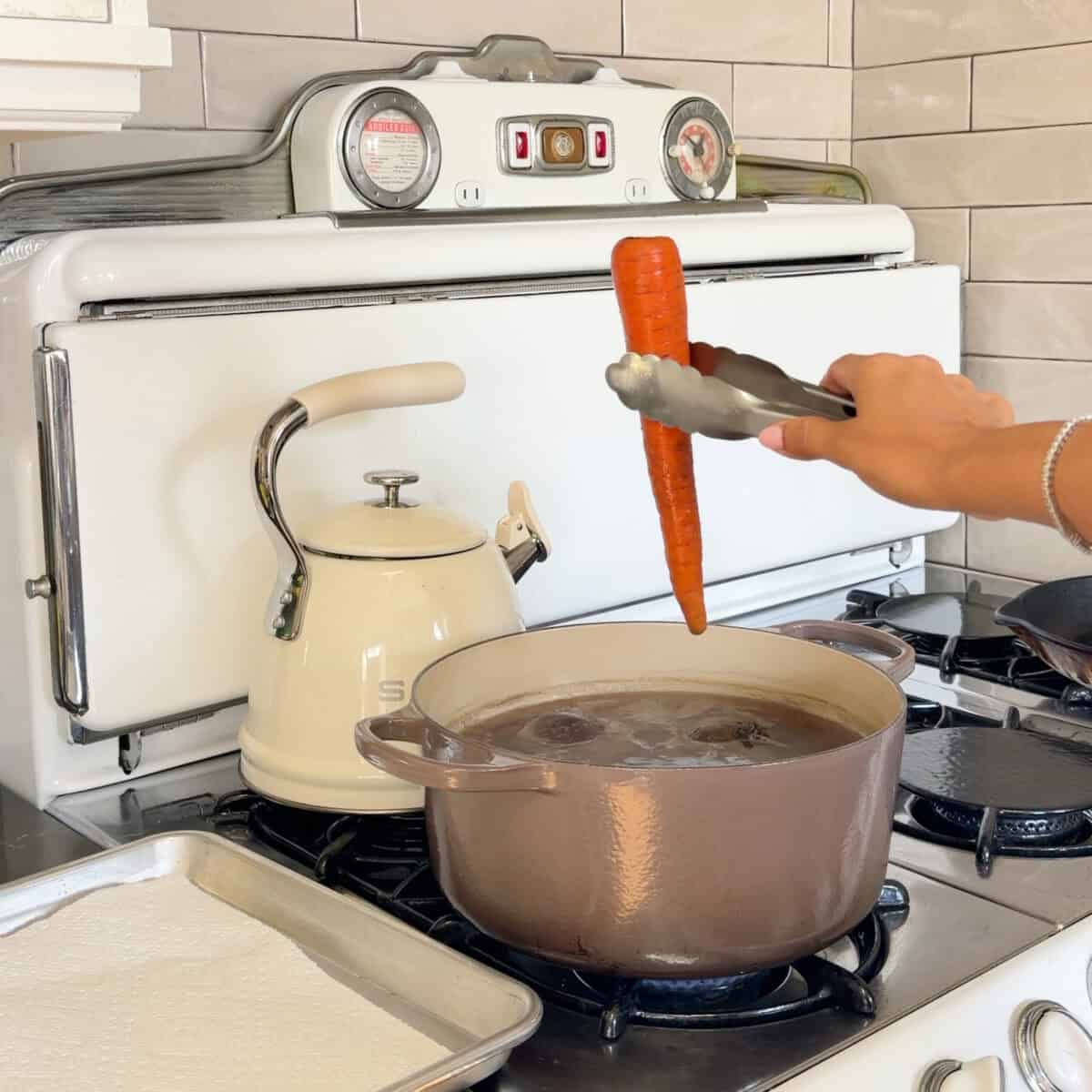Cooked whole carrot being removed from the boiling water.