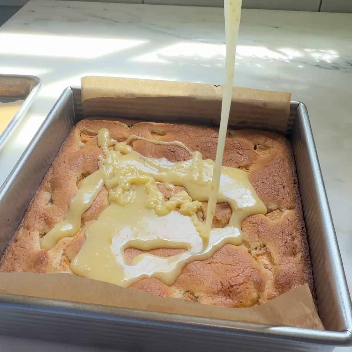 Pouring white chocolate peach glaze on cooled Peach Cobbler Brownies.