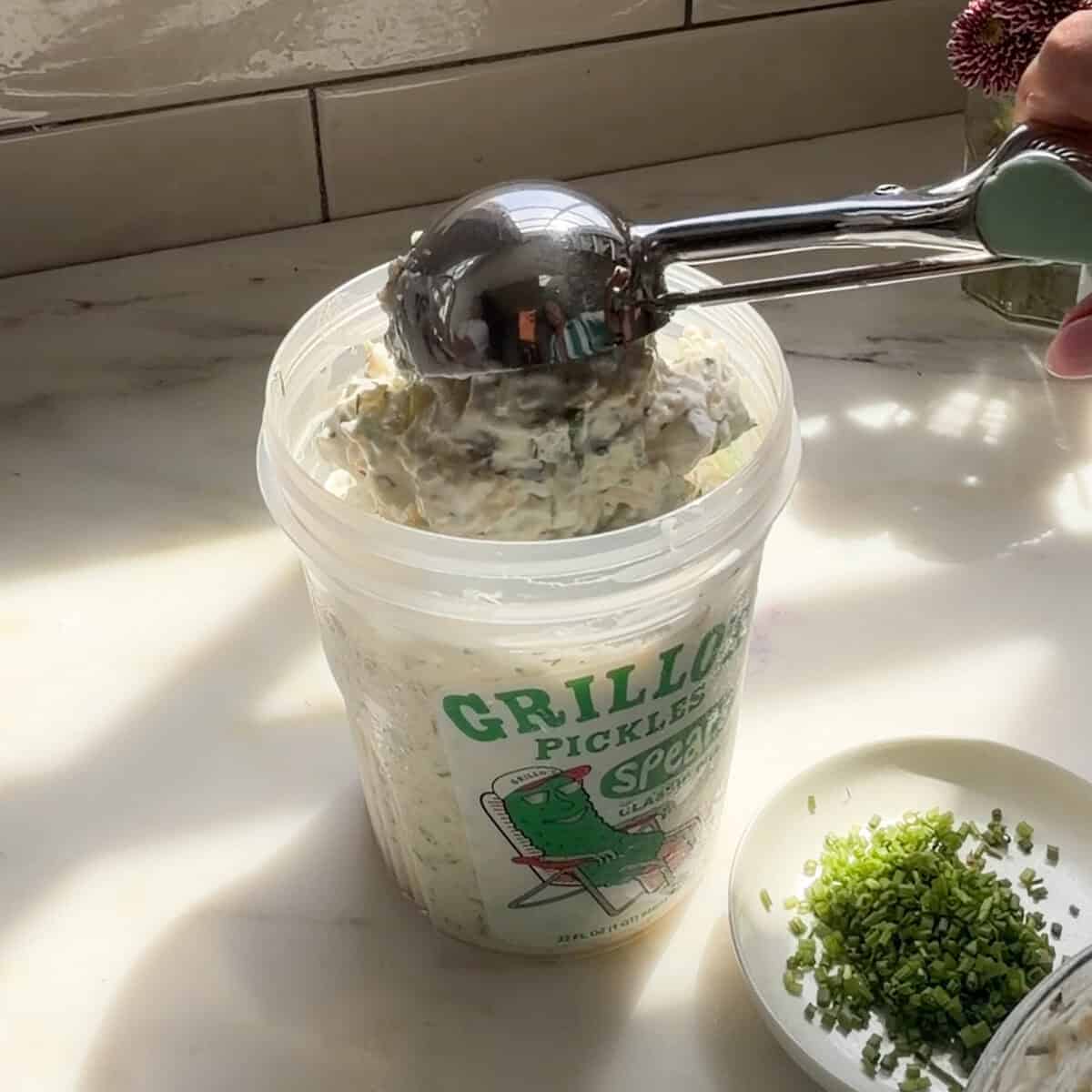 Scooping pickle dip into Grillo's Pickles container.