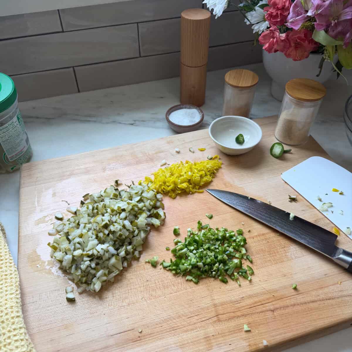 Chopped pickles, jalapeรฑo, and pepperoncini on cutting board.