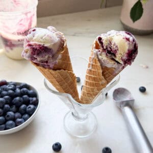 Melty ice cream cones in a sundae cup with blueberries in a bowl.