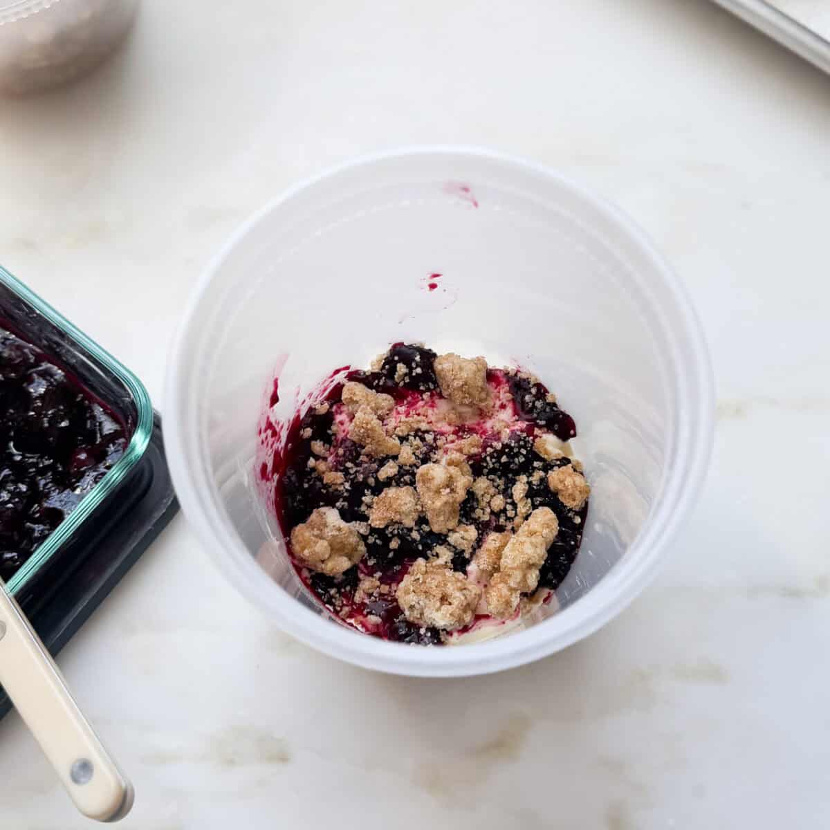 Layers of ice cream, blueberry compote, and crumble in a quart deli container.