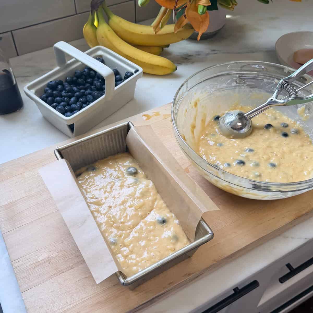 Blueberry banana bread batter in loaf pan next to large bowl of batter.