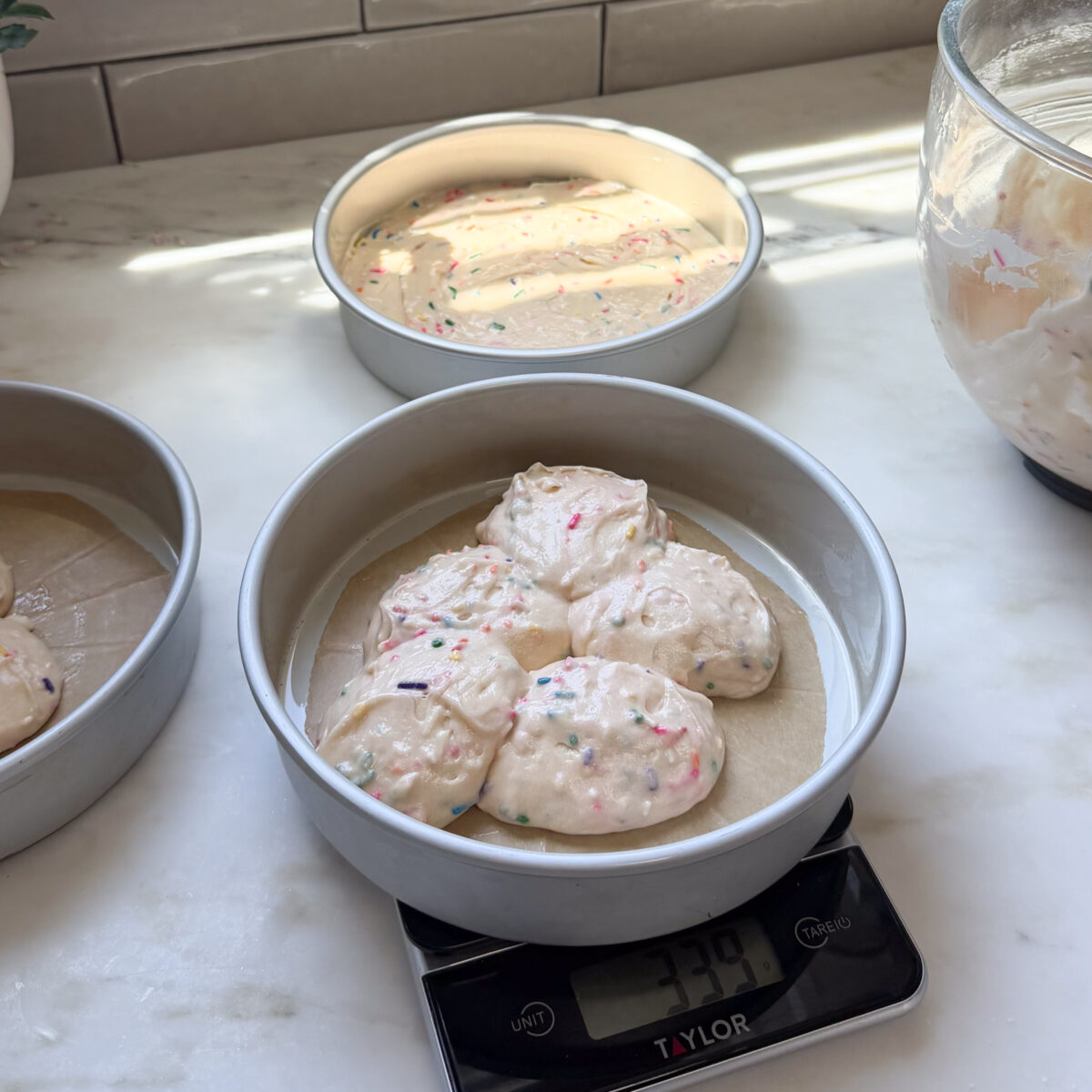 Scooping cake batter into prepared cake pans.