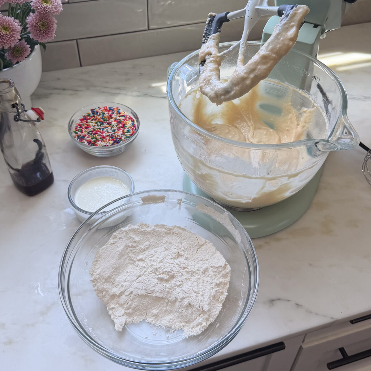 Large bowl of dry ingredients, buttermilk, and stand up mixer with cake batter.