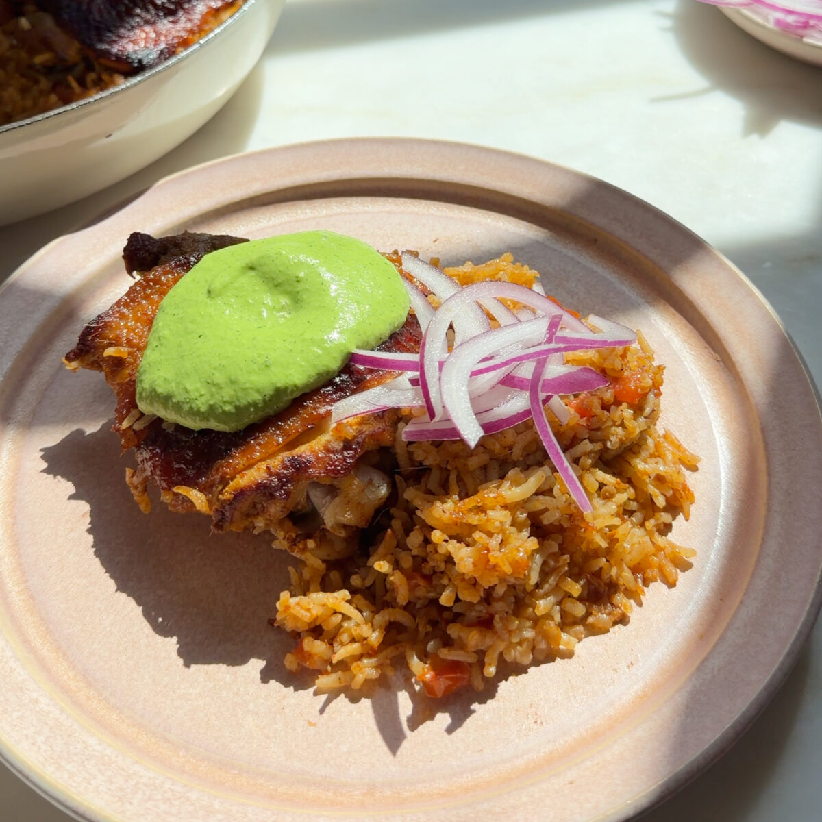 Plate of chicken and rice with aji verde and sliced red onion on top.