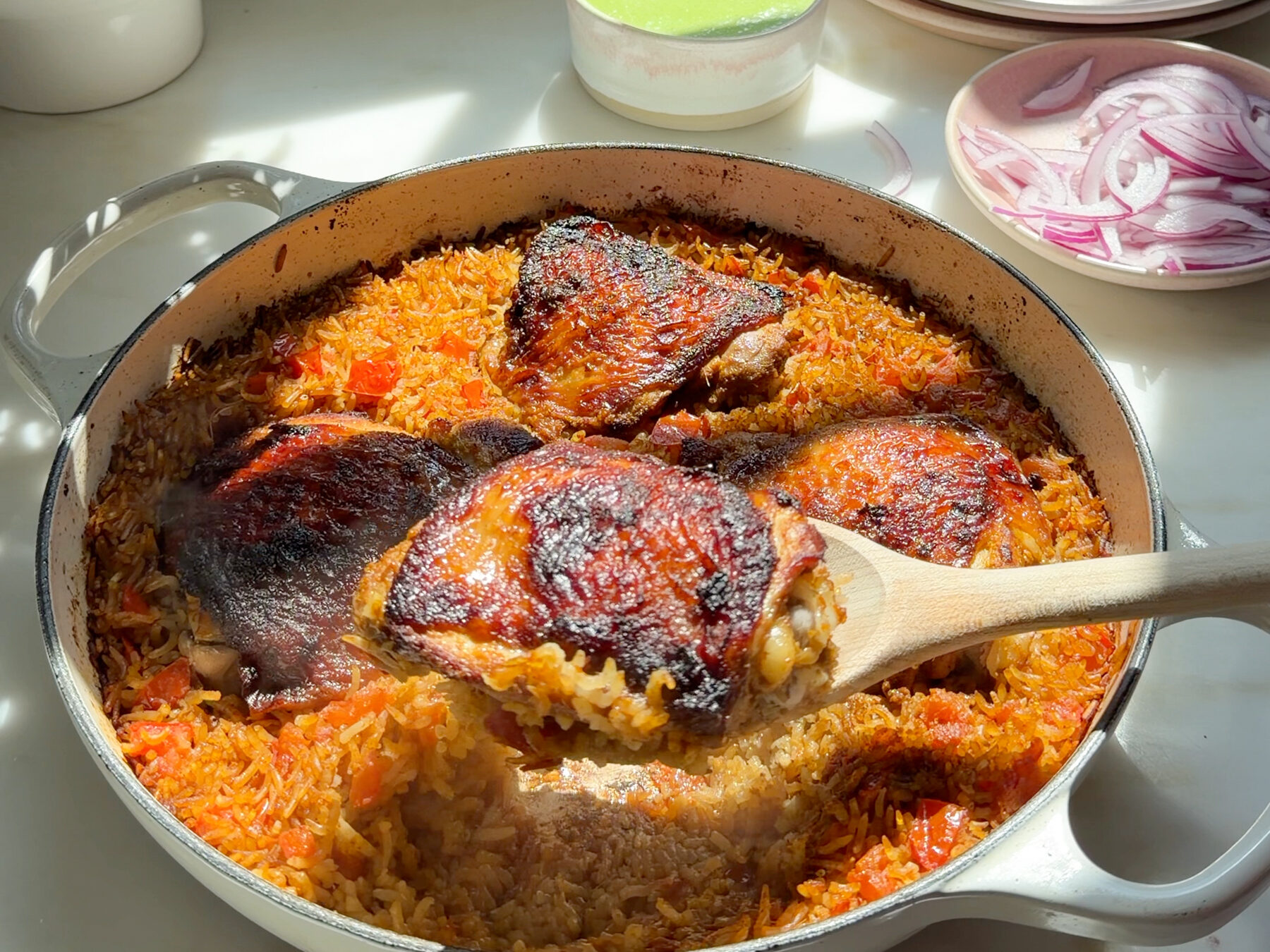 A spoon hold a chicken thigh, chicken and rice in braiser on counter.