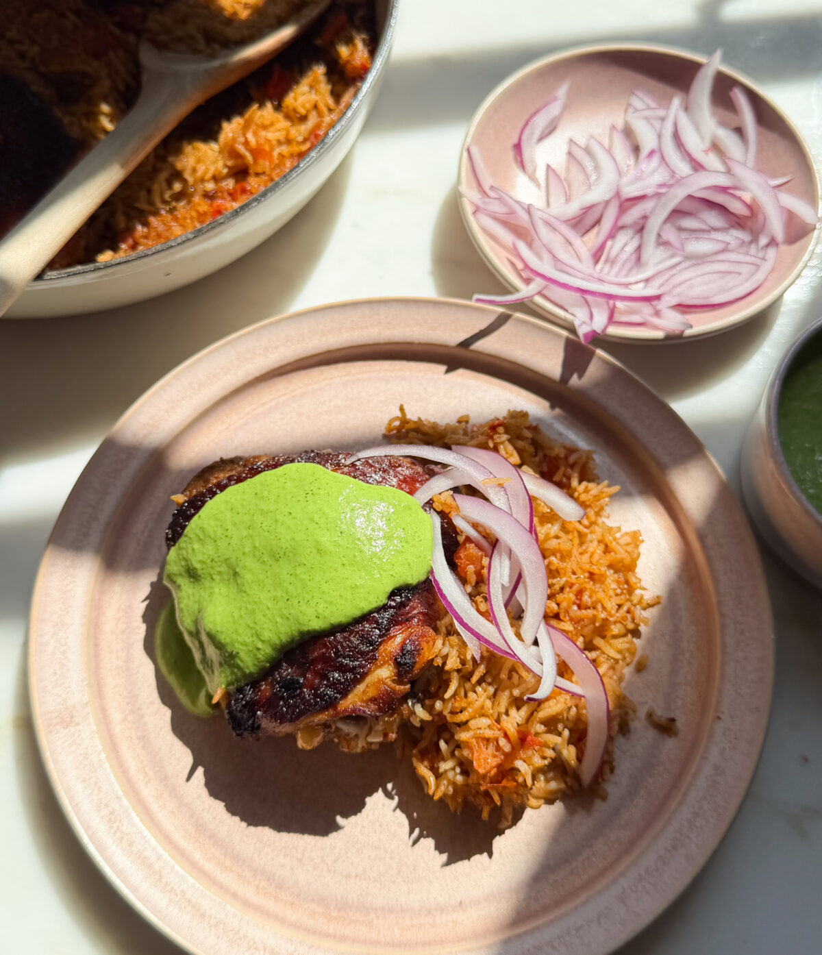 Chicken and rice on plate with aji verde and sliced onions on top.