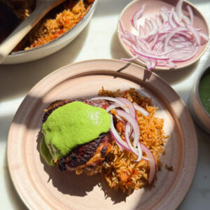 Chicken and rice on plate with aji verde and sliced onions on top.