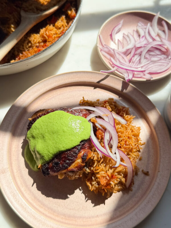Chicken and rice on plate with aji verde and sliced onions on top.