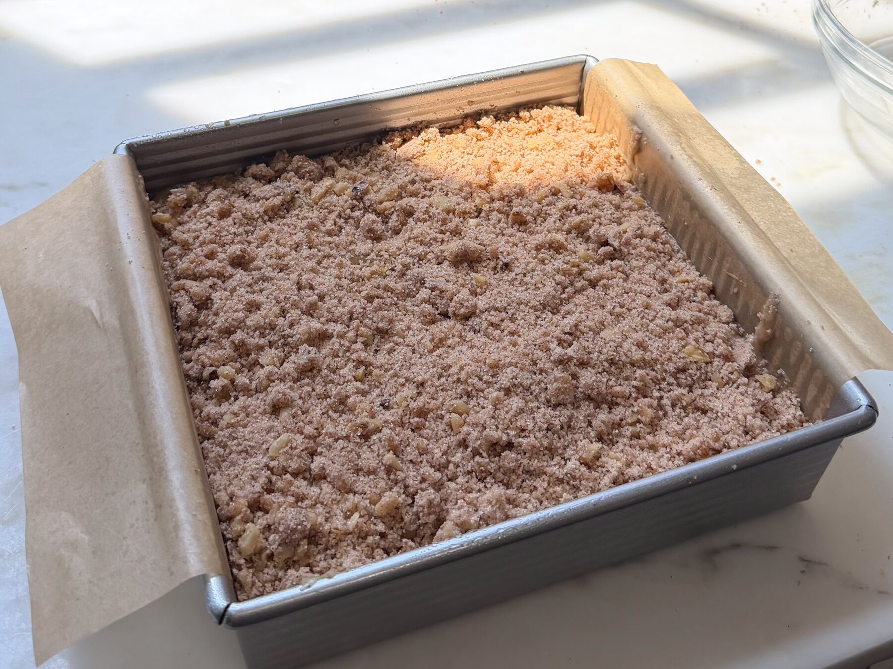 Banana bread coffee cake batter layered with walnut streusel in baking pan.