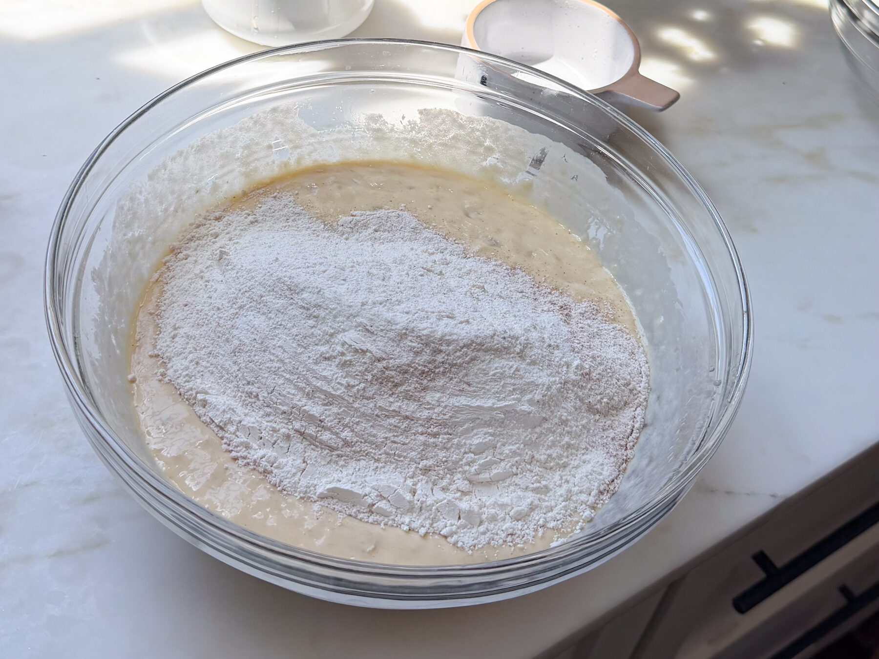 Dry ingredients atop wet ingredients for banana bread coffee cake batter in large bowl.