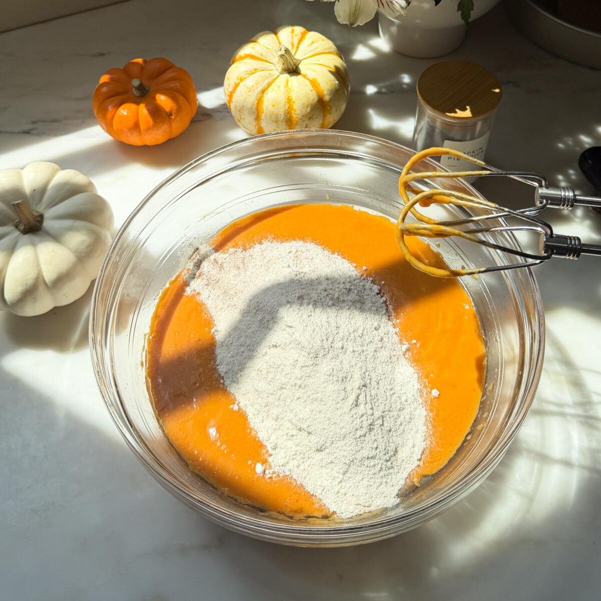 Dry ingredients added to wet ingredients in large bowl next to hand mixer.
