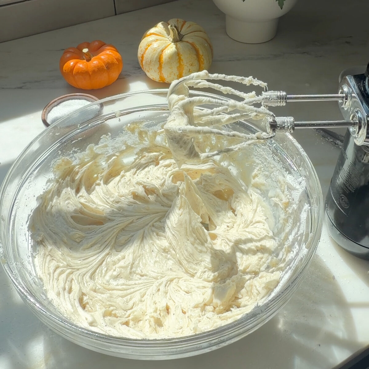 Brown butter frosting in large bowl next to hand mixer.