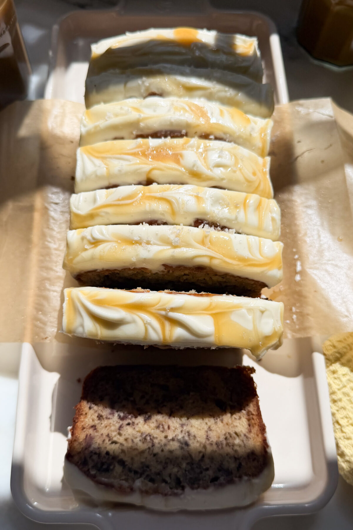 Frosted and sliced loaf of salted maple banana bread on a platter.