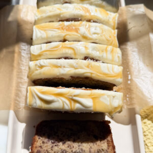 Frosted and sliced loaf of salted maple banana bread on a platter.