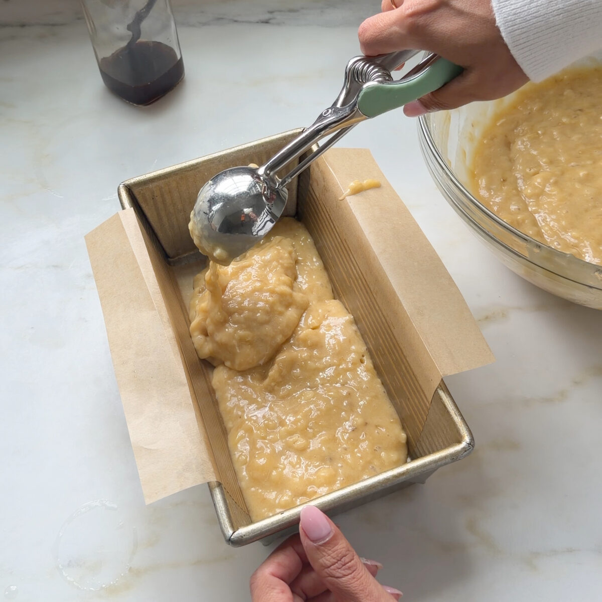 Scooping salted maple banana bread batter into prepared baking pan.