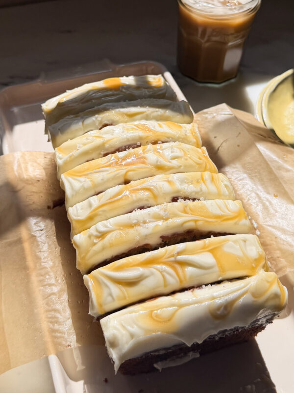 Frosted and sliced loaf of salted maple banana bread on a platter.
