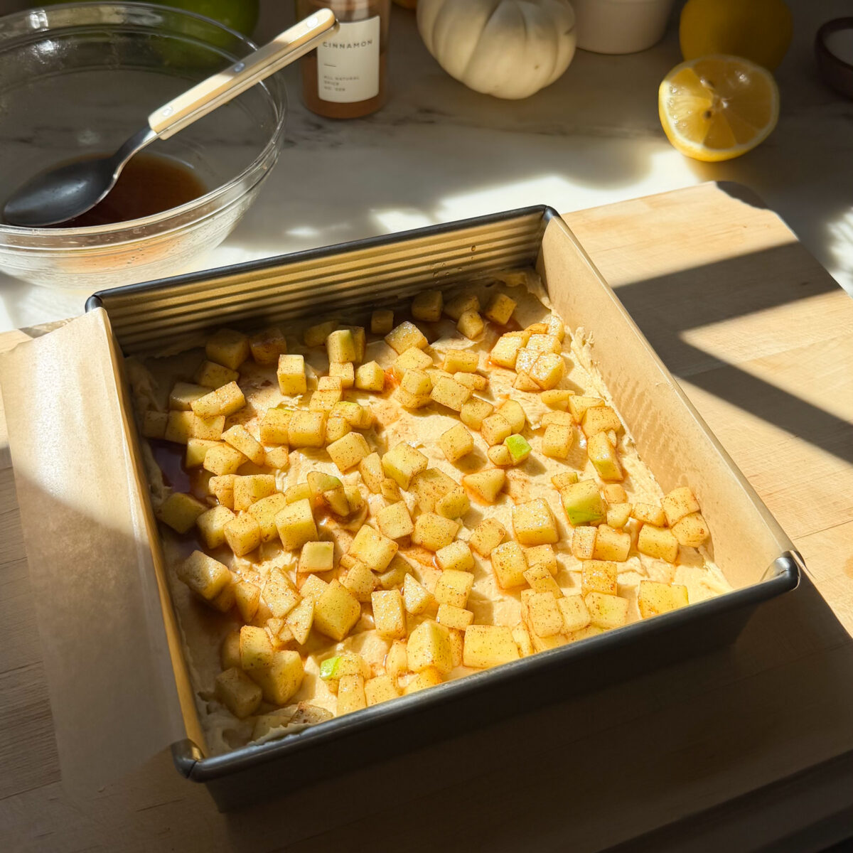 Cinnamon apples scattered on the surface of the batter in the baking pan.