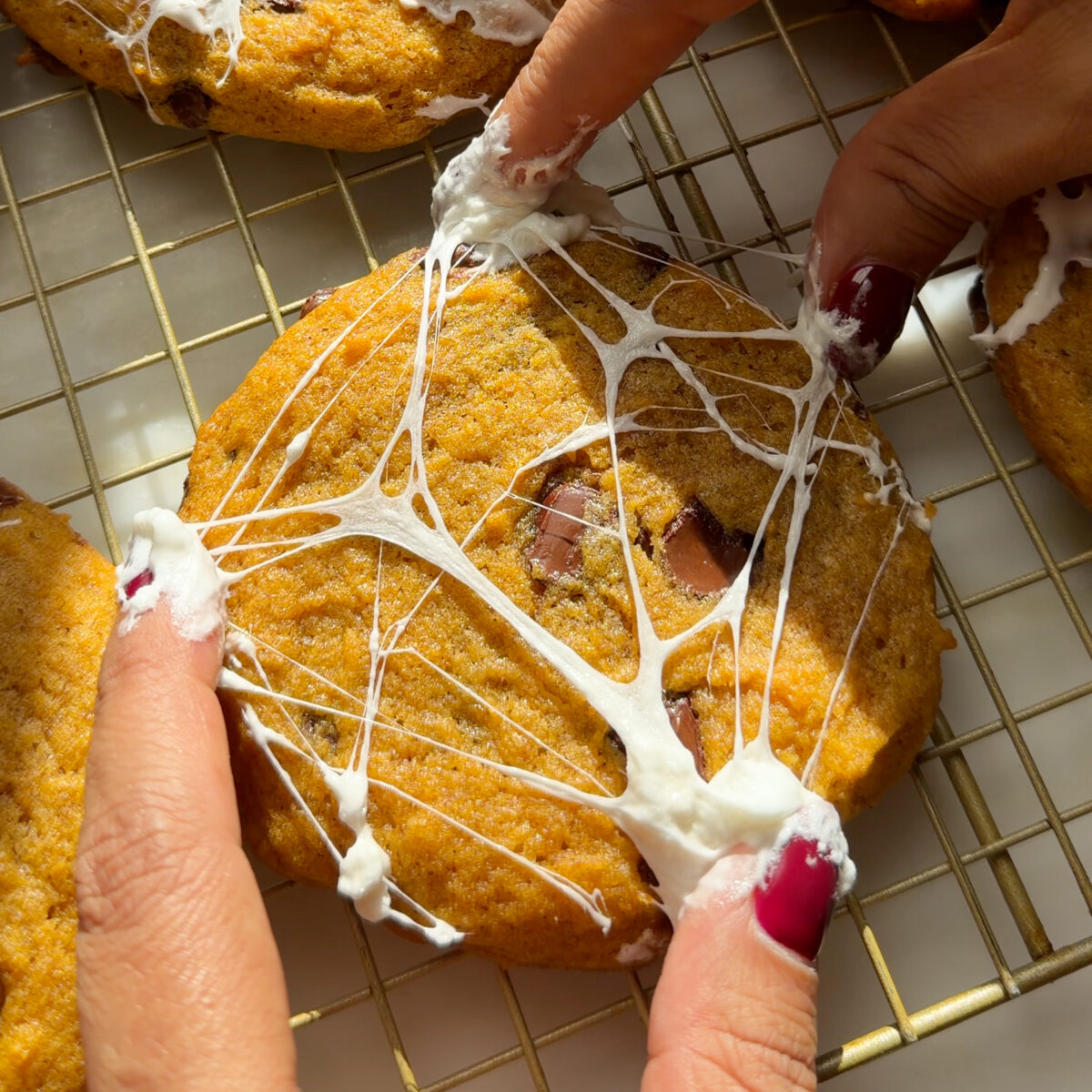 Adding marshmallow web to cookies on cooling rack.