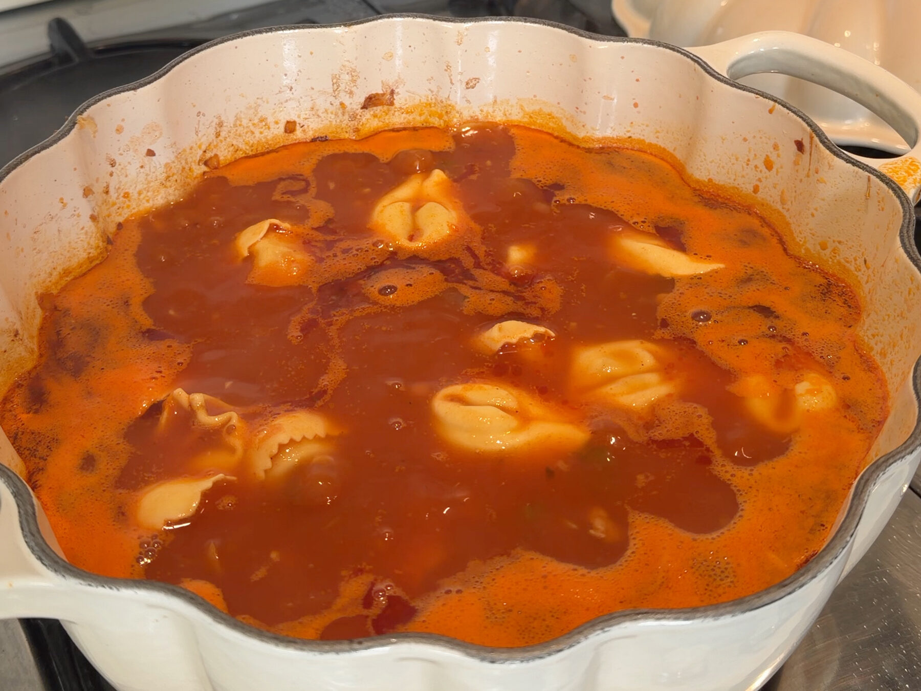 Pot of tortellini in tomato broth simmering on the stove.